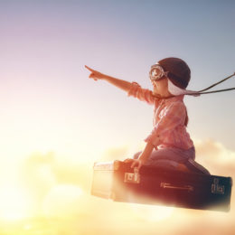 Child flying on a suitcase against the backdrop of a sunset.