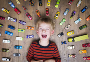 A boy laying on the floor surrounded by toy cars.